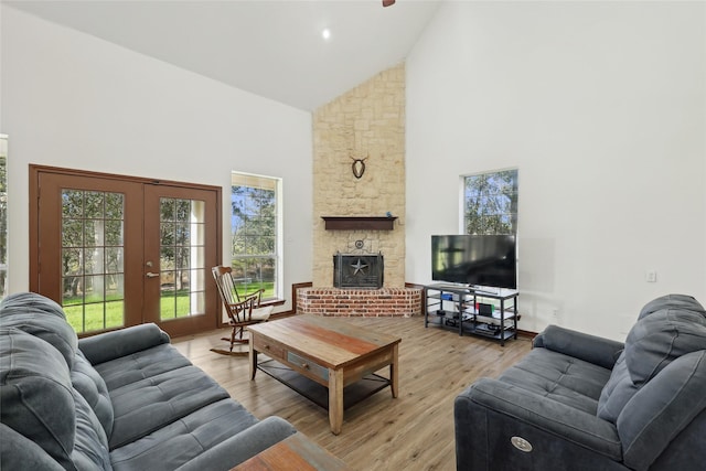 living room with a stone fireplace, light hardwood / wood-style flooring, high vaulted ceiling, and french doors