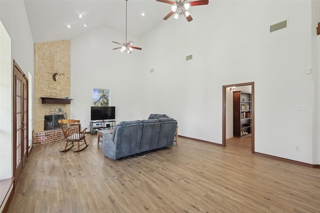 living room with a stone fireplace, high vaulted ceiling, ceiling fan, and light wood-type flooring