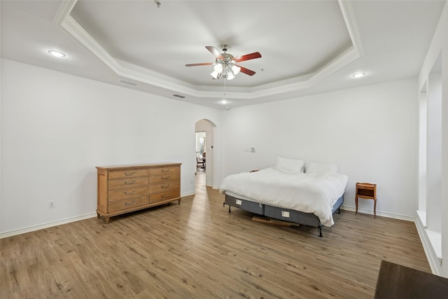 bedroom featuring wood-type flooring, ornamental molding, ceiling fan, and a tray ceiling