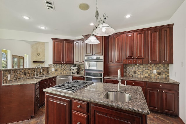 kitchen with pendant lighting, an island with sink, appliances with stainless steel finishes, and sink