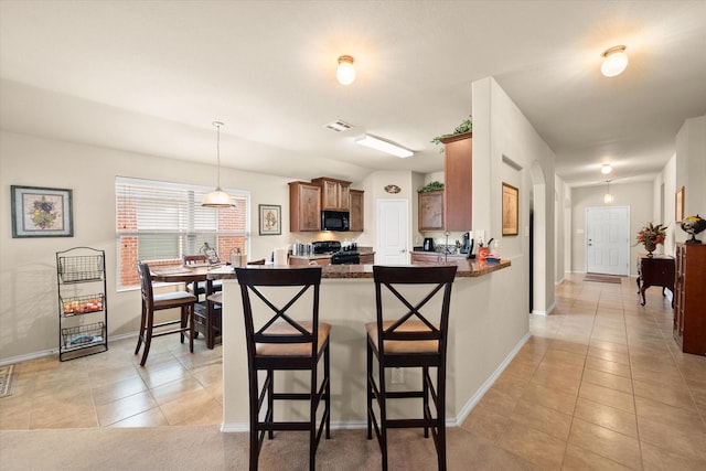 kitchen with pendant lighting, light tile patterned floors, black appliances, a kitchen bar, and kitchen peninsula