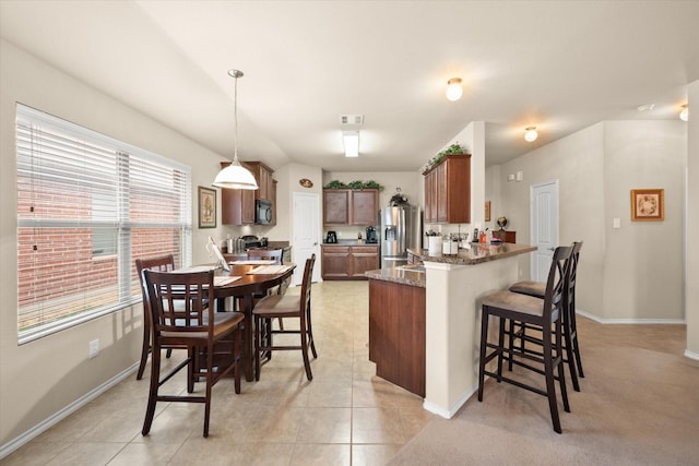 kitchen with decorative light fixtures, light tile patterned floors, dark stone countertops, appliances with stainless steel finishes, and kitchen peninsula