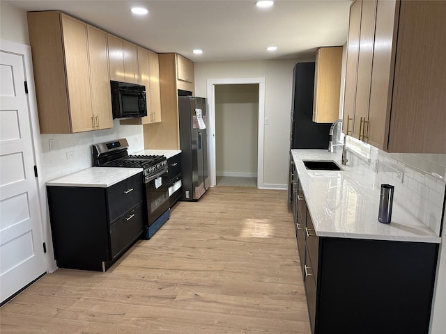 kitchen with appliances with stainless steel finishes, sink, backsplash, light brown cabinets, and light wood-type flooring