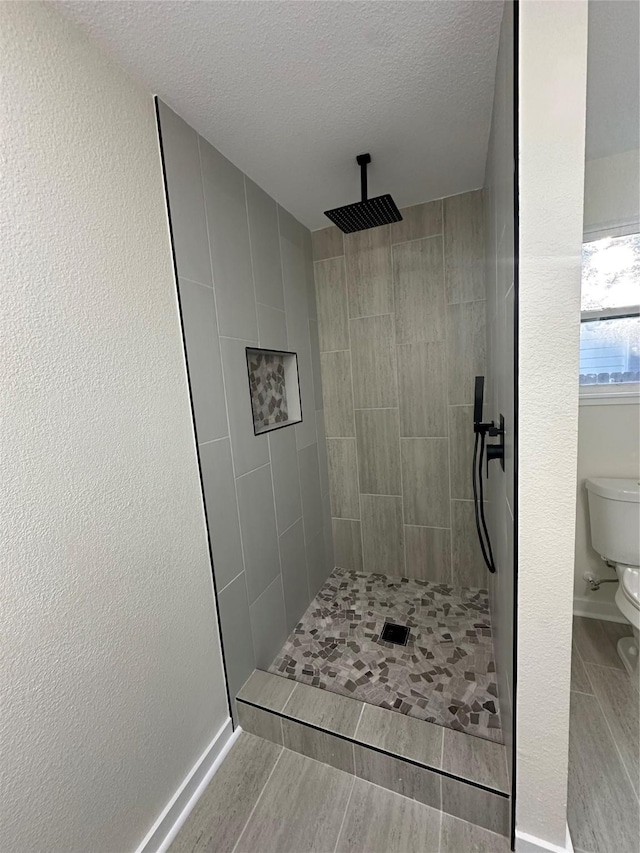 bathroom featuring toilet, a textured ceiling, and a tile shower