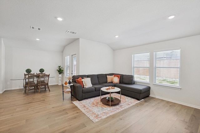 living room with vaulted ceiling, a textured ceiling, and light wood-type flooring