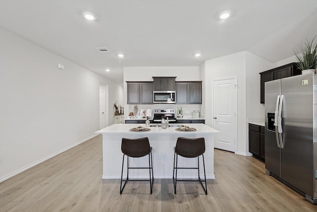 kitchen featuring a kitchen island with sink, dark brown cabinetry, stainless steel appliances, and light wood-type flooring