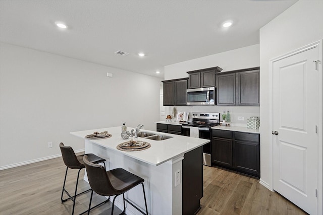 kitchen with a kitchen bar, sink, a center island with sink, light hardwood / wood-style flooring, and appliances with stainless steel finishes