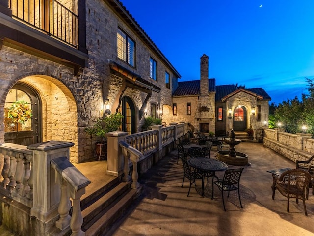 patio terrace at dusk featuring a balcony and a fireplace