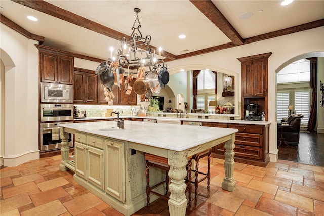 kitchen with built in microwave, tasteful backsplash, beamed ceiling, sink, and a kitchen island with sink