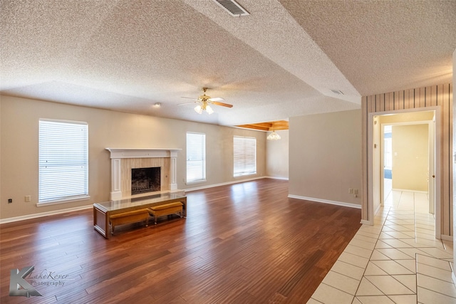 unfurnished living room featuring ceiling fan with notable chandelier, a fireplace, hardwood / wood-style floors, and a textured ceiling