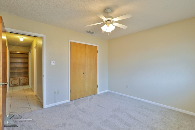 unfurnished bedroom featuring ceiling fan, light colored carpet, a closet, and a textured ceiling