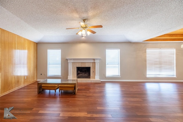 unfurnished living room with wood walls, a textured ceiling, dark hardwood / wood-style flooring, a tile fireplace, and ceiling fan