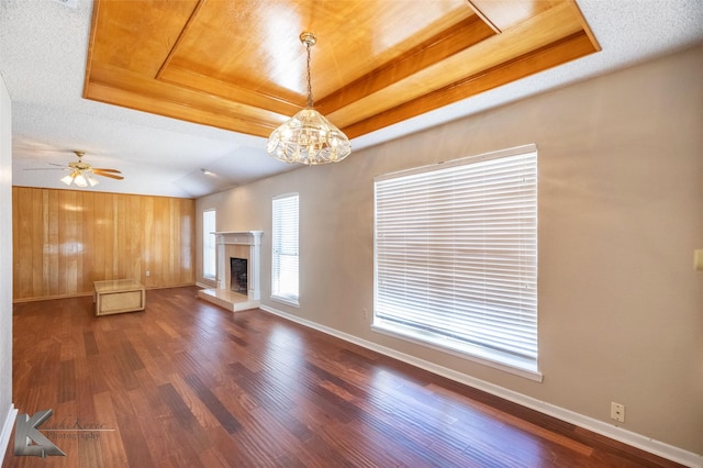 unfurnished living room featuring dark wood-type flooring, a raised ceiling, ceiling fan with notable chandelier, and a textured ceiling