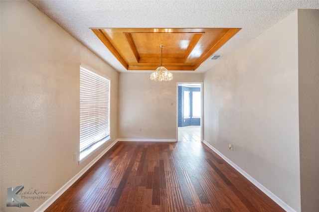 unfurnished room featuring dark hardwood / wood-style flooring, a raised ceiling, a textured ceiling, and a notable chandelier