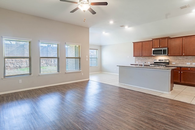 kitchen featuring tasteful backsplash, light hardwood / wood-style flooring, appliances with stainless steel finishes, ceiling fan, and a kitchen island with sink