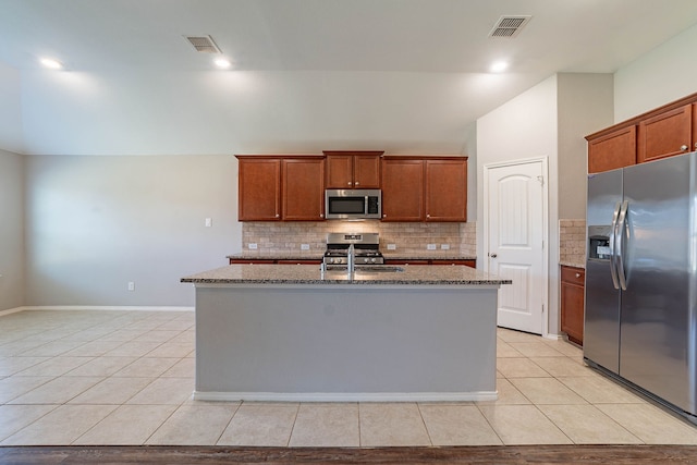 kitchen with stainless steel appliances, light stone counters, tasteful backsplash, an island with sink, and light tile patterned flooring