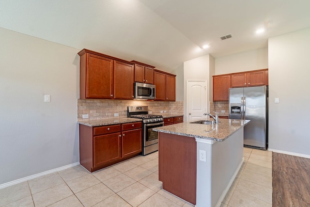 kitchen with sink, appliances with stainless steel finishes, light stone counters, a center island with sink, and decorative backsplash