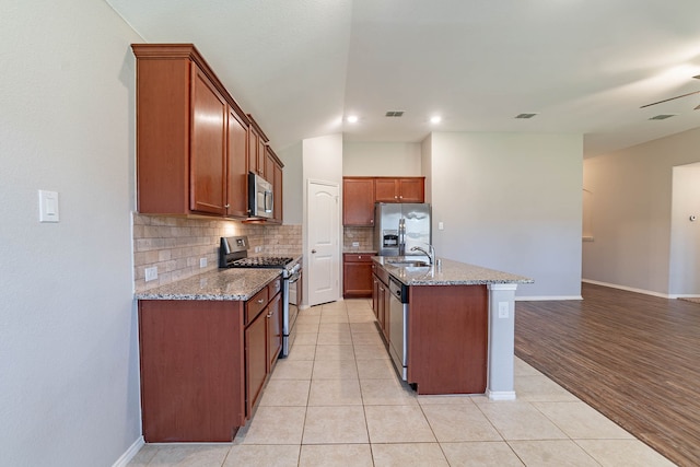 kitchen featuring sink, light stone counters, appliances with stainless steel finishes, an island with sink, and backsplash