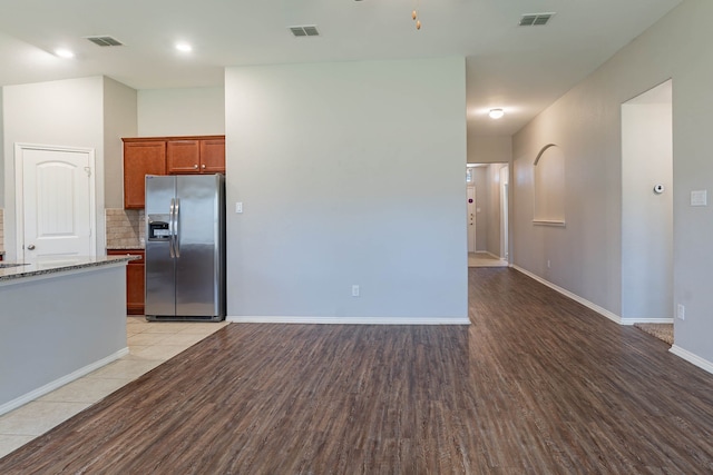 kitchen featuring dark stone counters, stainless steel fridge, decorative backsplash, and light hardwood / wood-style flooring