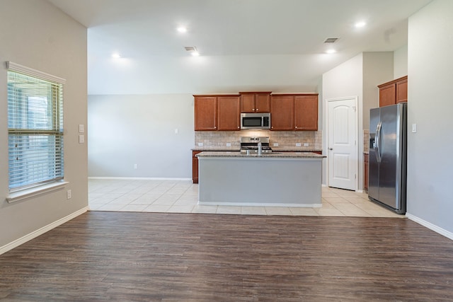 kitchen featuring light tile patterned floors, stainless steel appliances, a kitchen island with sink, and backsplash