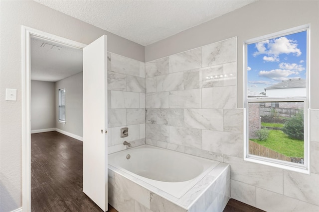 bathroom with tiled tub, hardwood / wood-style flooring, and a textured ceiling