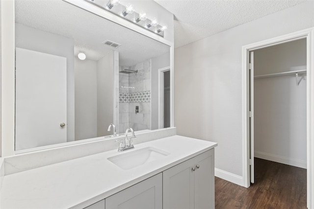 bathroom featuring vanity, a textured ceiling, wood-type flooring, and tiled shower