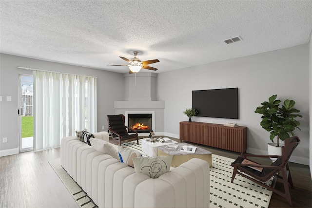 living room featuring wood-type flooring, a textured ceiling, ceiling fan, and a fireplace