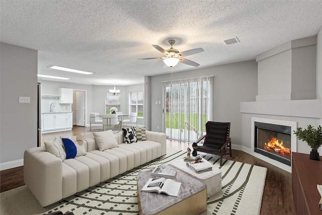 living room with dark wood-type flooring, ceiling fan with notable chandelier, and a textured ceiling