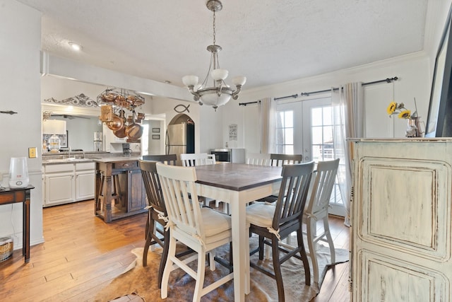 dining area featuring light wood-type flooring, french doors, crown molding, and a textured ceiling