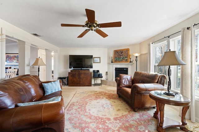 living room featuring ceiling fan, a tiled fireplace, and ornate columns