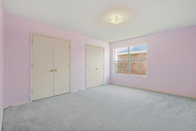 unfurnished bedroom with multiple closets, light colored carpet, and a textured ceiling