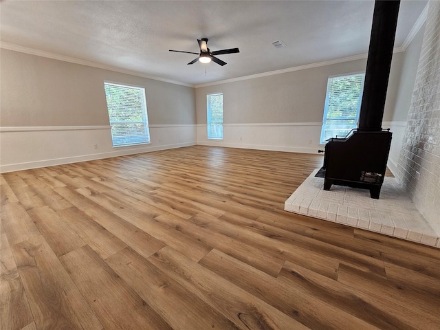 unfurnished living room featuring plenty of natural light, ornamental molding, light hardwood / wood-style floors, and a wood stove