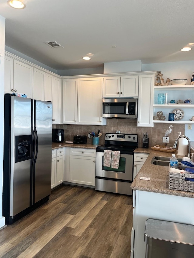 kitchen with appliances with stainless steel finishes, dark hardwood / wood-style floors, white cabinetry, sink, and backsplash