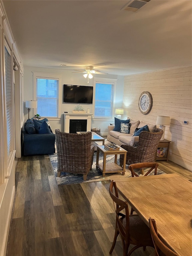 living room with a fireplace, dark wood finished floors, visible vents, wood walls, and ceiling fan