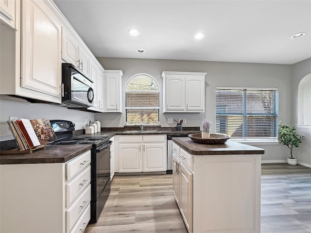 kitchen with sink, black appliances, white cabinets, a kitchen island, and light wood-type flooring