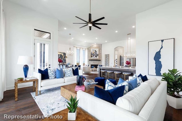 living room featuring wood-type flooring, a stone fireplace, and ceiling fan with notable chandelier