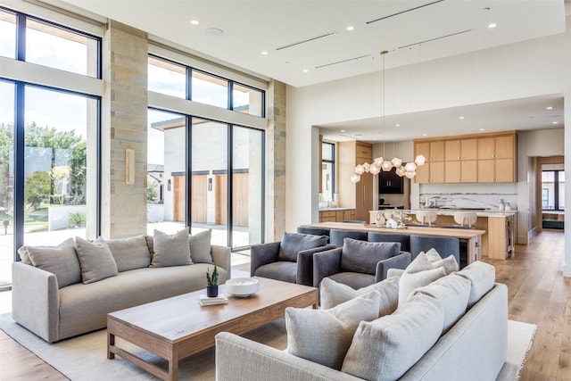 living room featuring a towering ceiling, a wealth of natural light, a chandelier, and light hardwood / wood-style flooring