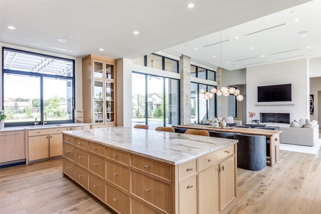 kitchen featuring sink, light stone counters, a kitchen island, a fireplace, and light hardwood / wood-style floors