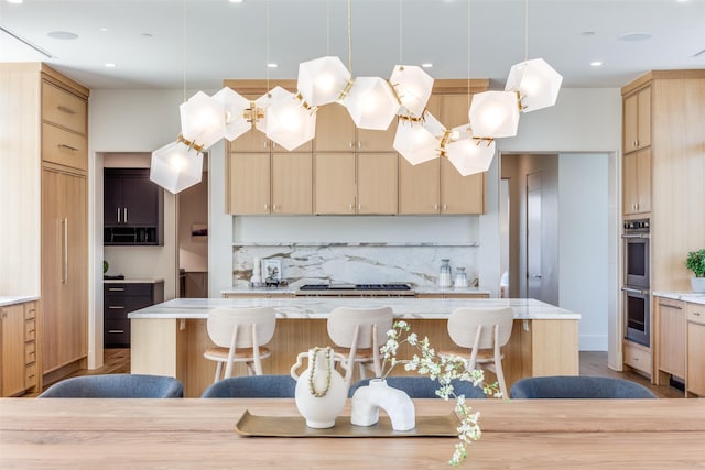 kitchen featuring a kitchen bar, gas stovetop, hanging light fixtures, light brown cabinets, and double oven