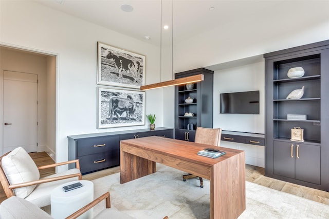 home office with built in shelves and light hardwood / wood-style flooring