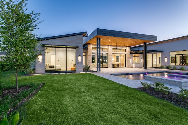 back house at dusk with a swimming pool with hot tub, a lawn, and a patio area