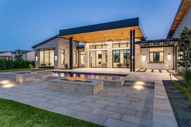 back house at dusk featuring an in ground hot tub, a patio area, and a fire pit