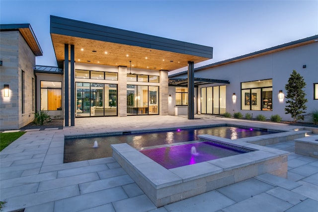 pool at dusk with an in ground hot tub and a patio