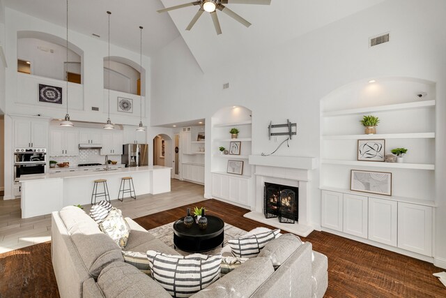 living room with high vaulted ceiling, dark hardwood / wood-style floors, built in features, and ceiling fan