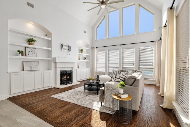 living room featuring a premium fireplace, high vaulted ceiling, built in features, and ceiling fan