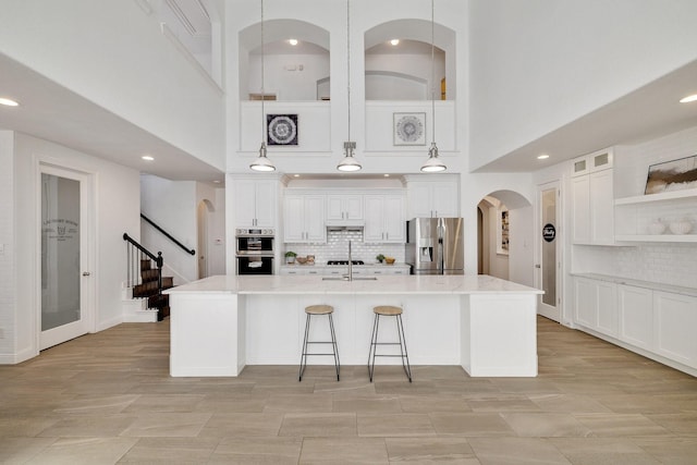 kitchen with light stone counters, stainless steel appliances, decorative light fixtures, and an island with sink