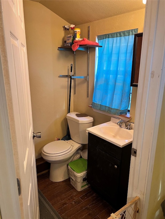 bathroom featuring wood-type flooring, lofted ceiling, vanity, and toilet