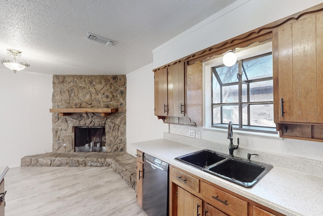 kitchen featuring sink, a textured ceiling, light wood-type flooring, dishwasher, and a fireplace