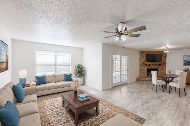 living room featuring ceiling fan, plenty of natural light, a fireplace, and light hardwood / wood-style flooring