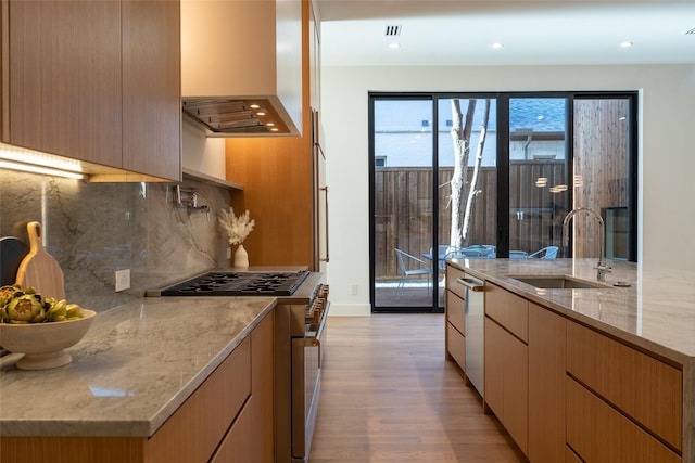 kitchen with appliances with stainless steel finishes, sink, exhaust hood, light stone counters, and light hardwood / wood-style floors